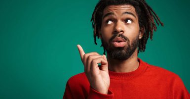 Portrait of confused african american man looking and pointing finger upward isolated over green background